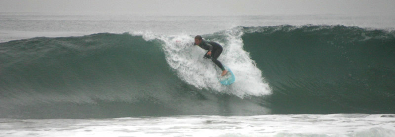 Surfer dropping into a blue wave at Sands Beach